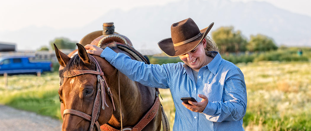 Woman smiling while walking with her horse and looking at her phone