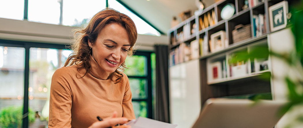 Woman working on papers in front of her laptop in her home office