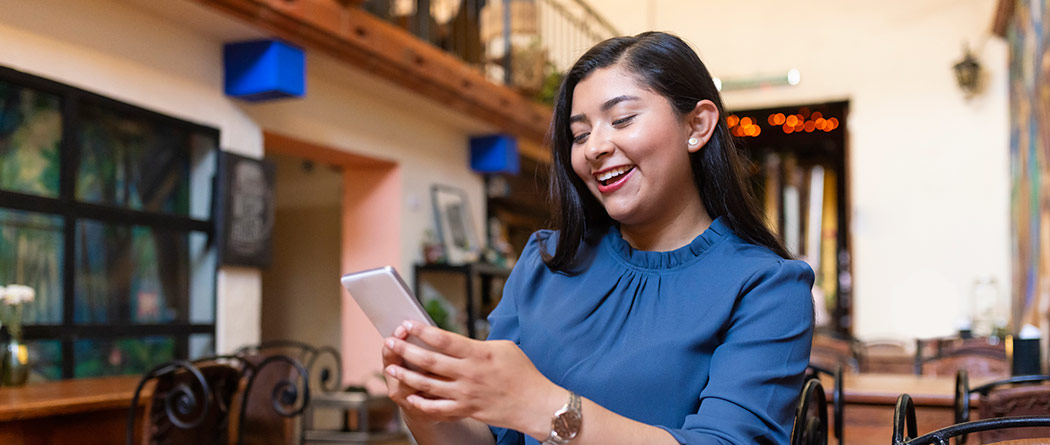 Woman smiling at a cafe while looking at her phone