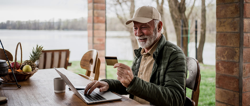 Man on his porch making a purchase on his laptop with a card