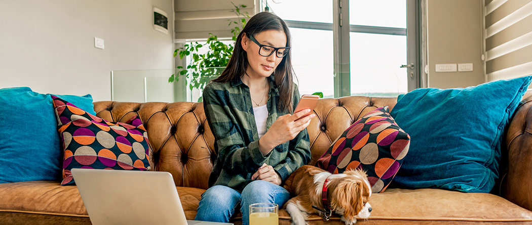 Woman looking at her phone while on her couch with her dog