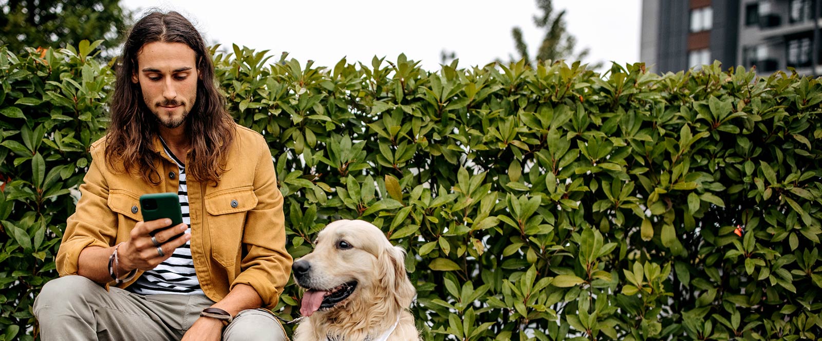 Man looking at his smart phone outside while his dog sits next to him