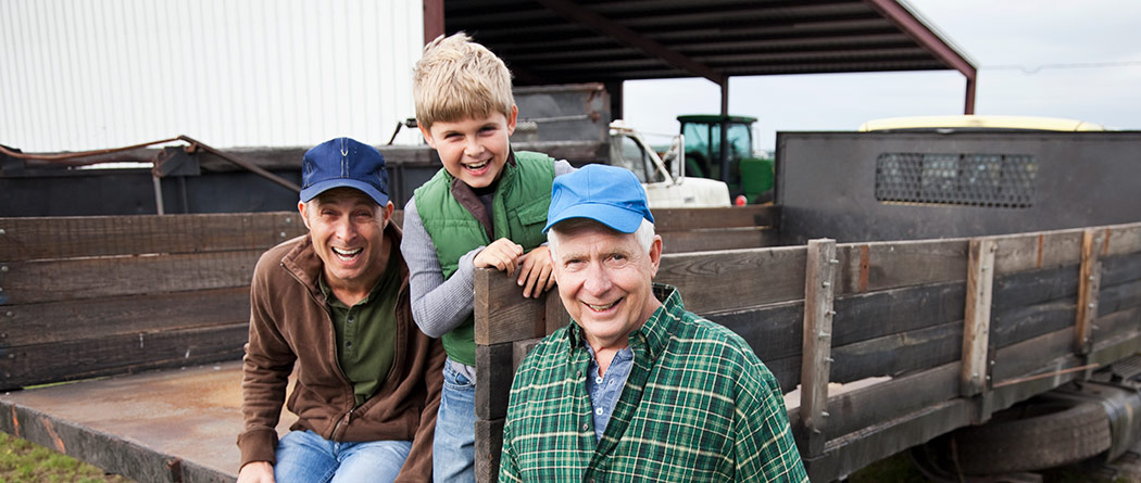 Three generations of farmers smiling together on back of truck